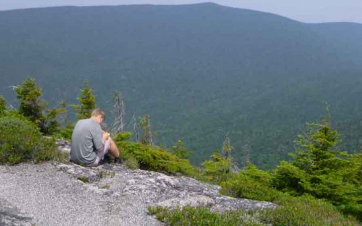 a person rests on a rock and writes in a journal while overlooking the maine Appalachian mountains